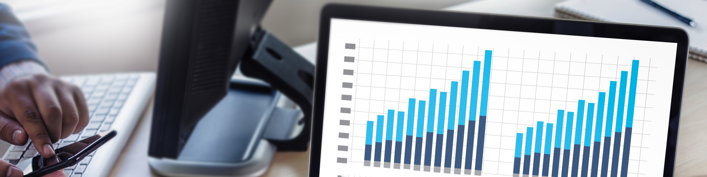 A person tapping their phone with a laptop showing data in the form of bar charts